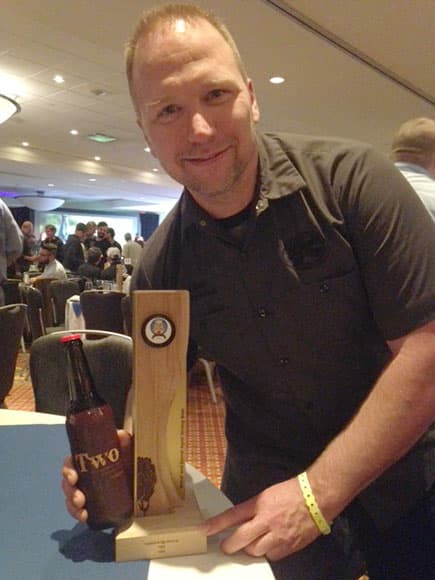 Covered Bridge Brewing owner John vanDyk holding a glass of the award-winning Two, alongside the gold medal trophy.